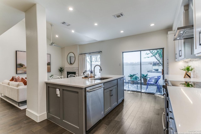 kitchen featuring dishwasher, sink, dark hardwood / wood-style flooring, a kitchen island with sink, and a fireplace