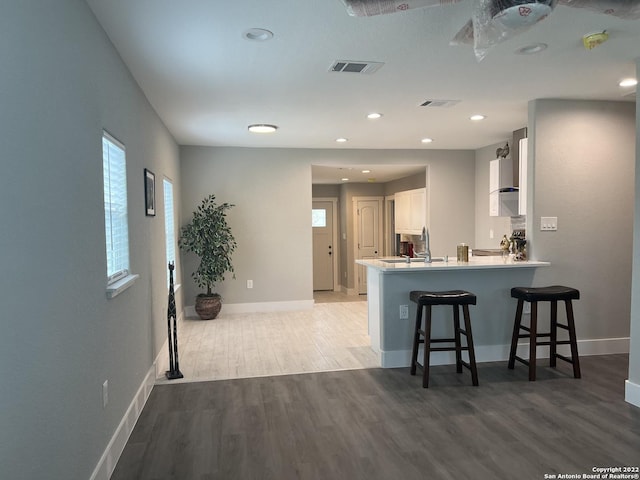 kitchen with kitchen peninsula, light wood-type flooring, a wealth of natural light, a breakfast bar, and white cabinetry