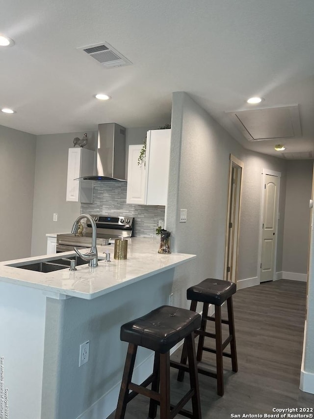 kitchen featuring stainless steel range with electric stovetop, wall chimney exhaust hood, a kitchen breakfast bar, and kitchen peninsula