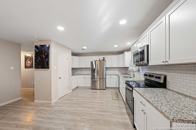 kitchen featuring sink, light wood-type flooring, appliances with stainless steel finishes, light stone counters, and white cabinetry