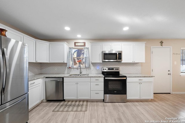 kitchen with white cabinets, stainless steel appliances, light stone counters, and sink