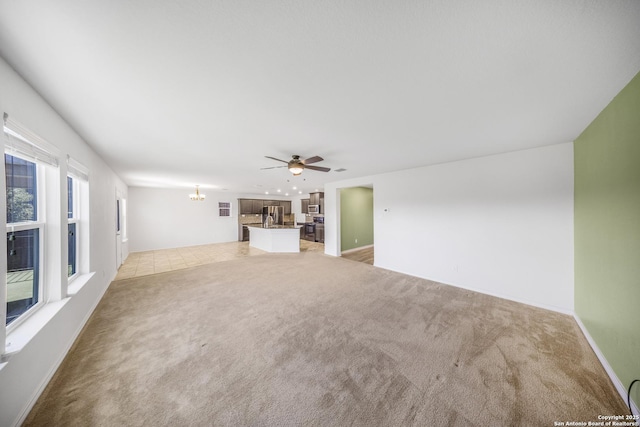 unfurnished living room featuring ceiling fan with notable chandelier and light colored carpet