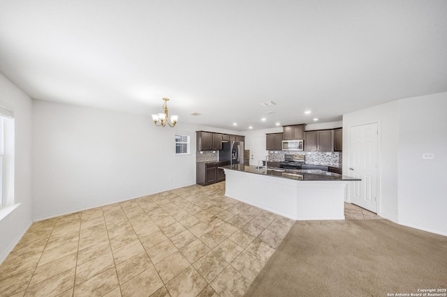 kitchen with decorative backsplash, dark brown cabinetry, stainless steel appliances, a center island with sink, and an inviting chandelier