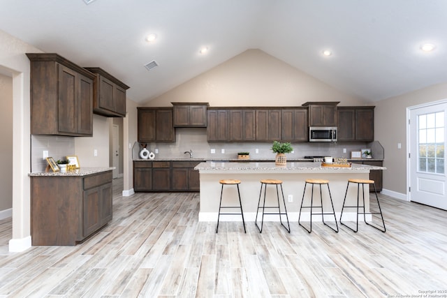 kitchen with light stone countertops, backsplash, a kitchen island, and dark brown cabinetry