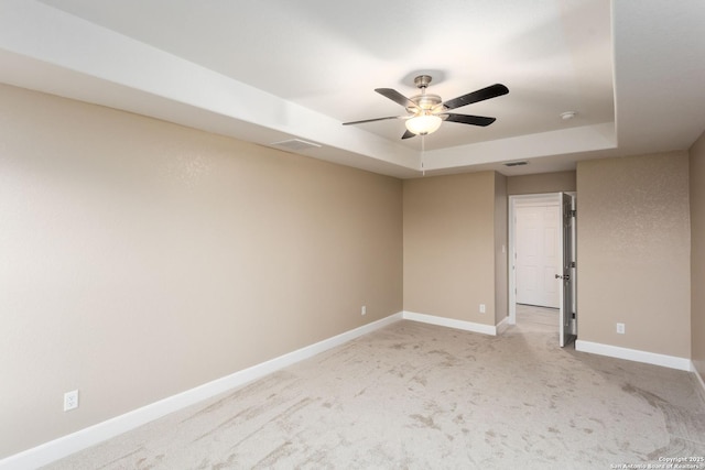 empty room featuring light carpet, a raised ceiling, and ceiling fan