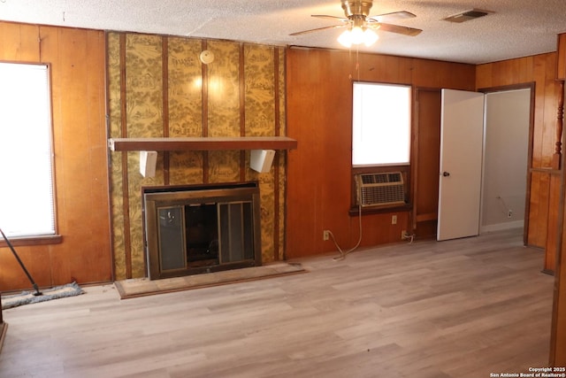 unfurnished living room with cooling unit, light hardwood / wood-style flooring, ceiling fan, and wooden walls