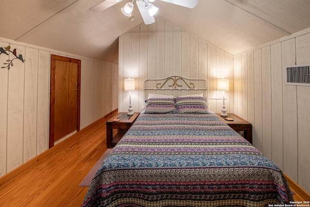 bedroom featuring hardwood / wood-style flooring, vaulted ceiling, ceiling fan, and wood walls