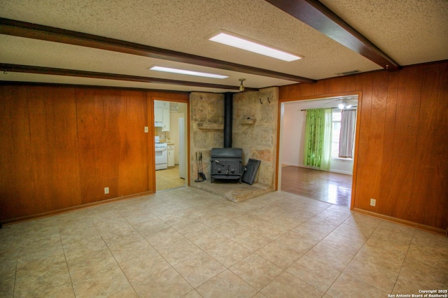 unfurnished living room featuring a textured ceiling, wood walls, a wood stove, and beam ceiling