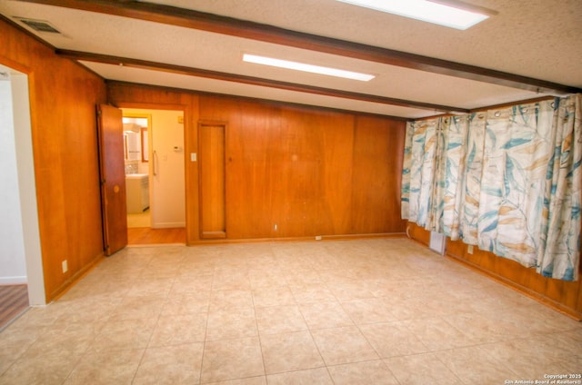 tiled empty room featuring wood walls, a textured ceiling, and beam ceiling