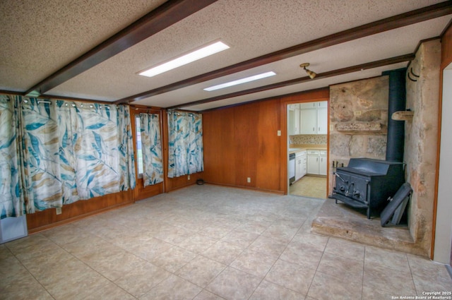 unfurnished room featuring a textured ceiling, wood walls, a wood stove, and beamed ceiling