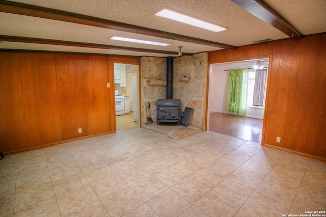 unfurnished living room with a textured ceiling, a wood stove, wood walls, and beamed ceiling