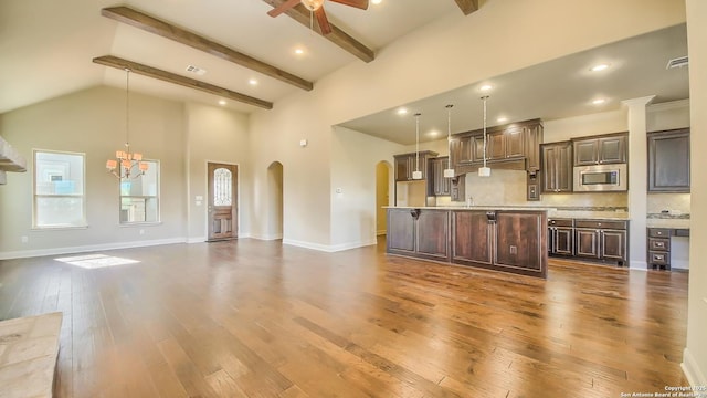 unfurnished living room with plenty of natural light, beamed ceiling, dark wood-type flooring, and ceiling fan with notable chandelier