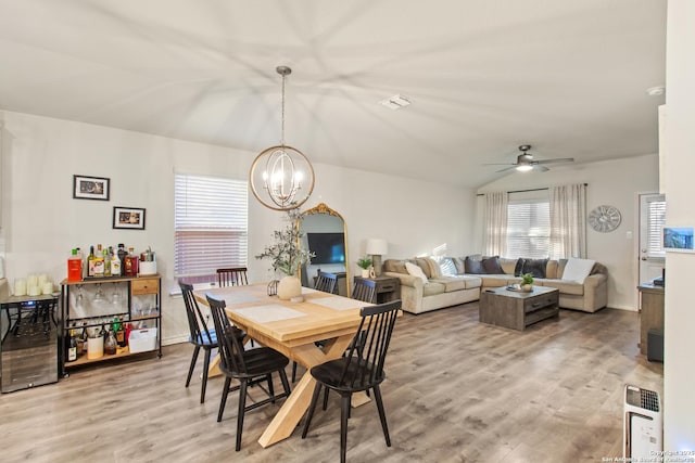 dining area with ceiling fan with notable chandelier, wood-type flooring, and beverage cooler