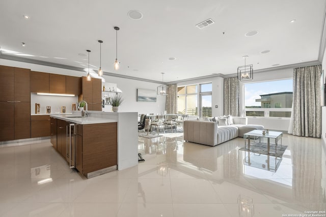 kitchen with pendant lighting, light tile patterned floors, crown molding, and an island with sink