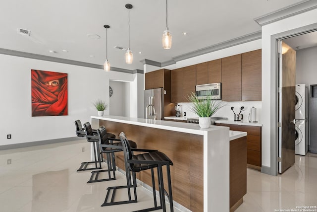 kitchen featuring a kitchen breakfast bar, hanging light fixtures, stacked washing maching and dryer, light tile patterned floors, and appliances with stainless steel finishes