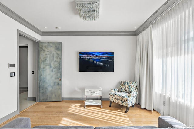 living area with hardwood / wood-style flooring, ornamental molding, and an inviting chandelier