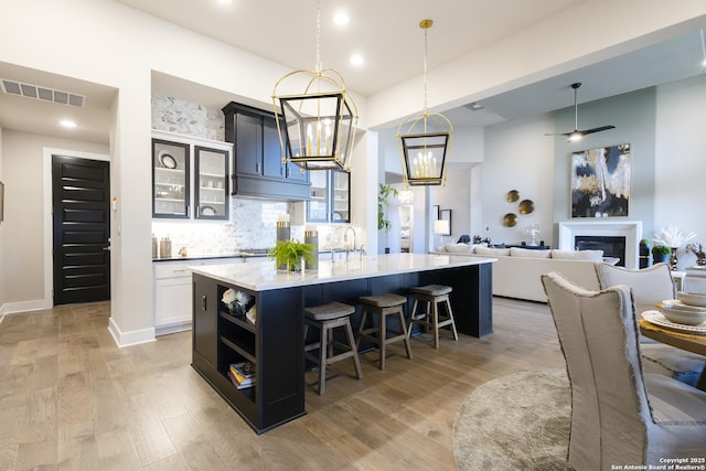 kitchen featuring a kitchen bar, tasteful backsplash, wood-type flooring, hanging light fixtures, and an island with sink