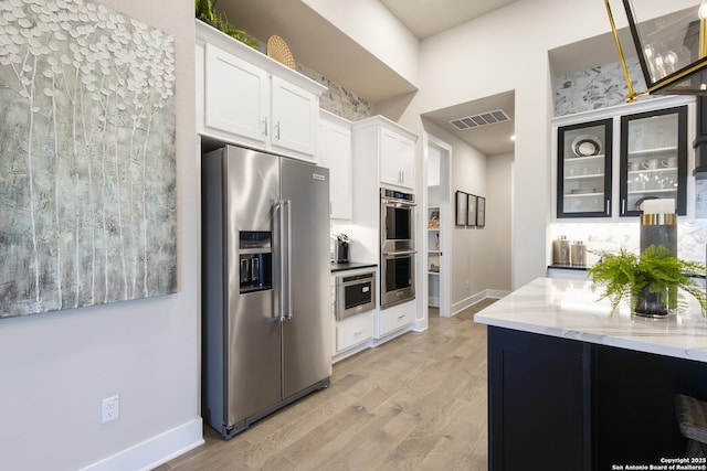 kitchen with light stone countertops, appliances with stainless steel finishes, light wood-type flooring, tasteful backsplash, and white cabinets