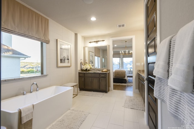 bathroom with a chandelier, vanity, a bathtub, and plenty of natural light