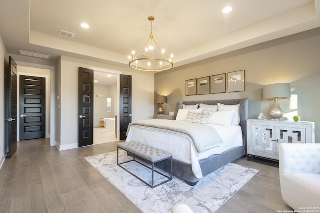 bedroom featuring an inviting chandelier, a raised ceiling, and hardwood / wood-style flooring