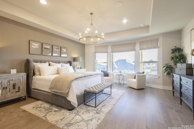 bedroom featuring hardwood / wood-style floors, a raised ceiling, and an inviting chandelier