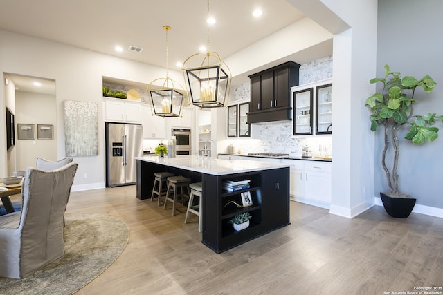 kitchen with sink, stainless steel appliances, backsplash, decorative light fixtures, and a center island with sink