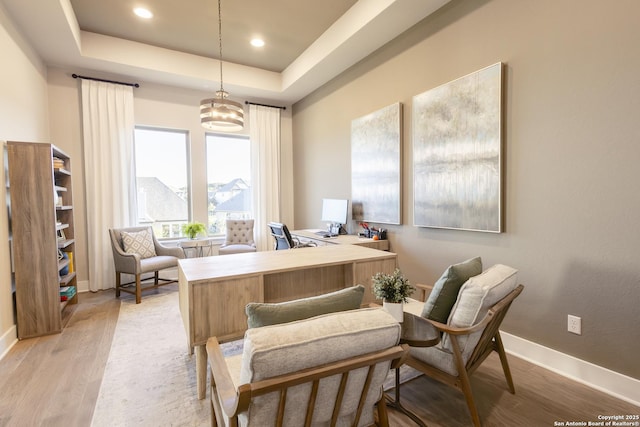 office area with a notable chandelier, a raised ceiling, and light wood-type flooring