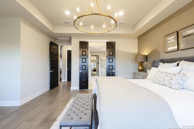 bedroom with a chandelier, wood-type flooring, and a tray ceiling