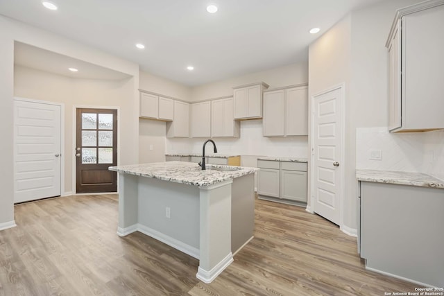 kitchen with light stone countertops, light hardwood / wood-style floors, and an island with sink