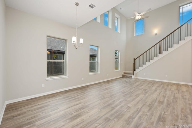 unfurnished living room with ceiling fan with notable chandelier, light wood-type flooring, and a high ceiling