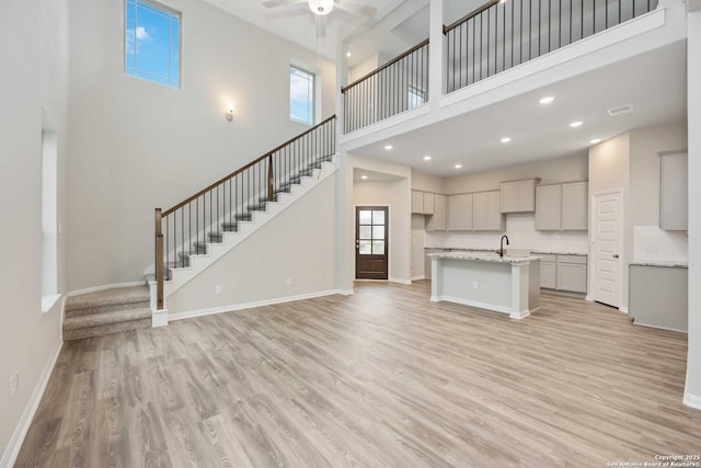 kitchen with gray cabinetry, a high ceiling, a center island with sink, ceiling fan, and light wood-type flooring