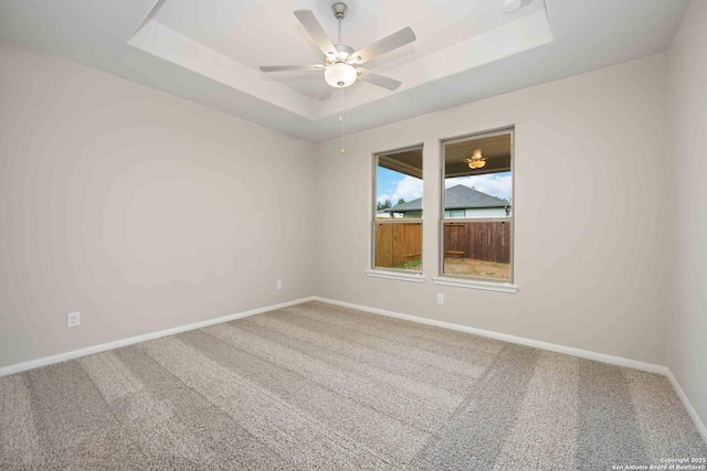 empty room featuring carpet, a tray ceiling, and ceiling fan