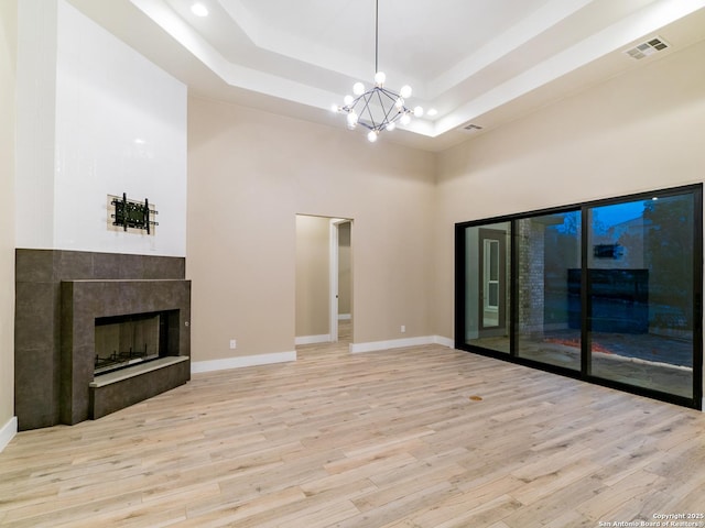 unfurnished living room featuring light hardwood / wood-style flooring, a notable chandelier, a fireplace, and a raised ceiling