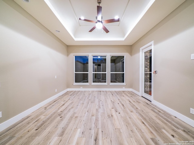 unfurnished room with ceiling fan, a tray ceiling, and light wood-type flooring