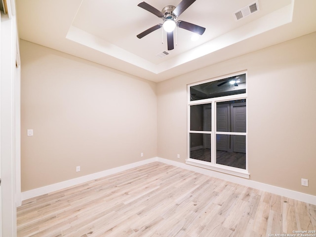 empty room with ceiling fan, a tray ceiling, and light wood-type flooring