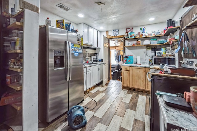 kitchen featuring appliances with stainless steel finishes, light stone counters, a textured ceiling, light brown cabinets, and white cabinets