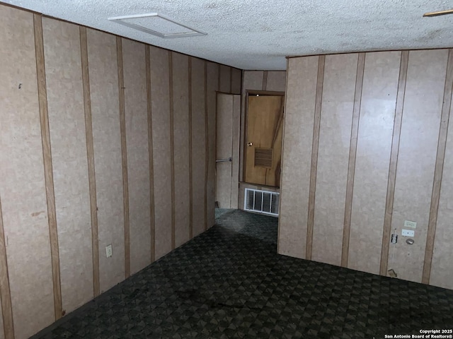 unfurnished room featuring a textured ceiling, carpet floors, and wooden walls