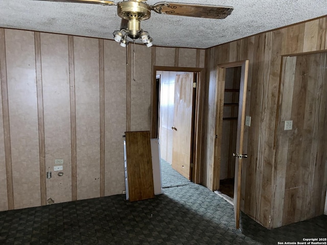 unfurnished room featuring ceiling fan, wood walls, a textured ceiling, and dark carpet