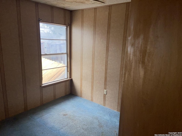 unfurnished room with carpet flooring, a textured ceiling, and wooden walls