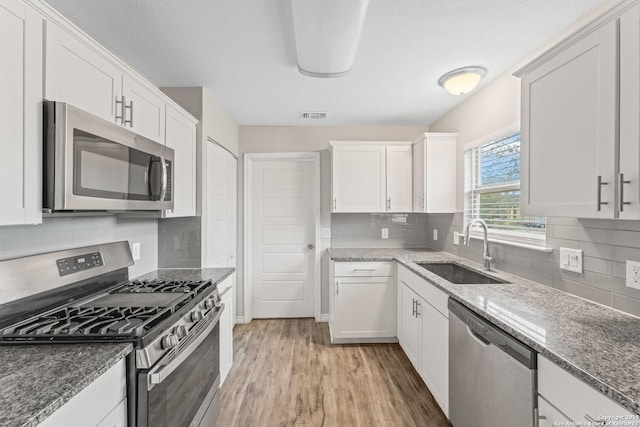 kitchen with stainless steel appliances, sink, dark stone countertops, and white cabinets