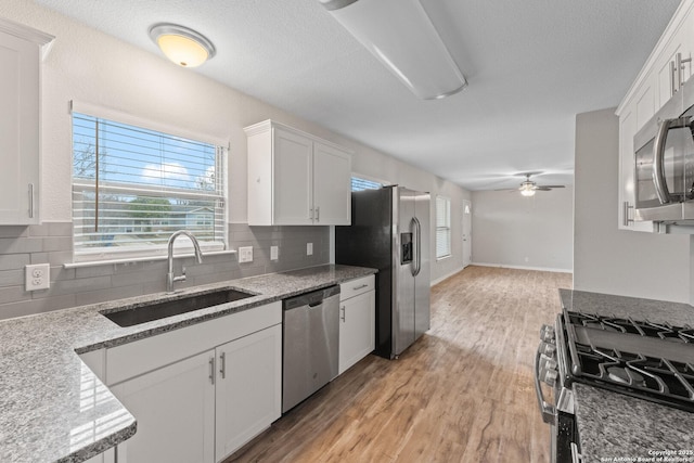 kitchen featuring sink, light stone counters, light hardwood / wood-style flooring, stainless steel appliances, and white cabinets