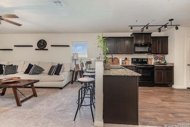 kitchen featuring black appliances, sink, light stone counters, dark brown cabinetry, and a breakfast bar area