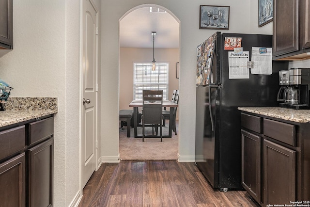 kitchen with black fridge, dark hardwood / wood-style floors, decorative light fixtures, light stone counters, and dark brown cabinetry