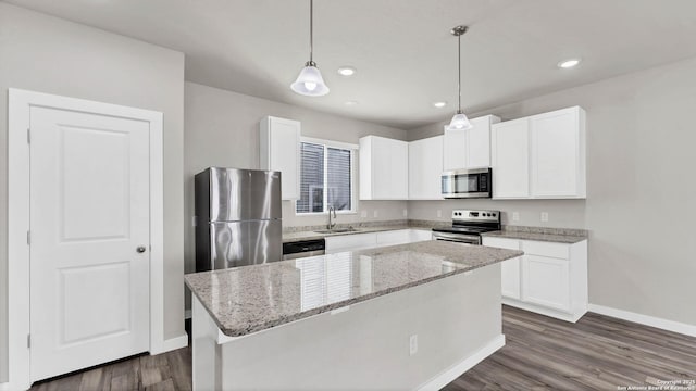 kitchen with appliances with stainless steel finishes, pendant lighting, a kitchen island, sink, and white cabinetry