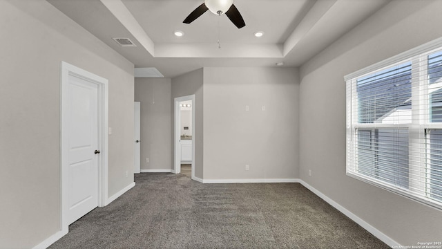 unfurnished bedroom featuring a raised ceiling, ceiling fan, and dark carpet