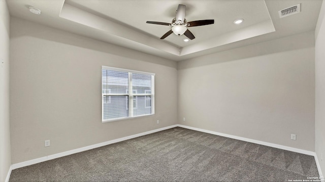 spare room with ceiling fan, dark colored carpet, and a tray ceiling