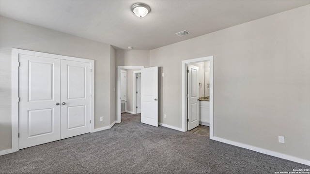 unfurnished bedroom with a closet, connected bathroom, and dark colored carpet