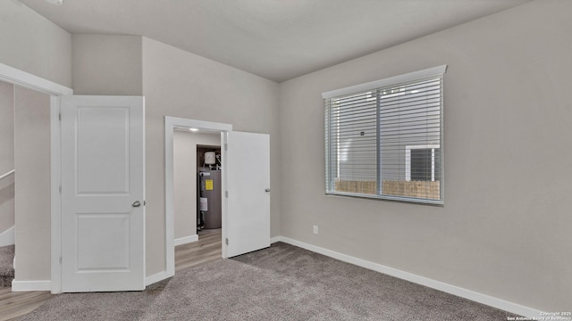 unfurnished bedroom with light colored carpet and water heater