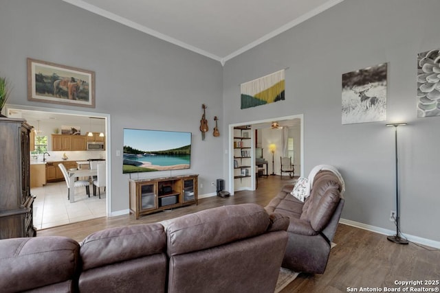 living room with crown molding, light hardwood / wood-style flooring, a towering ceiling, and ceiling fan