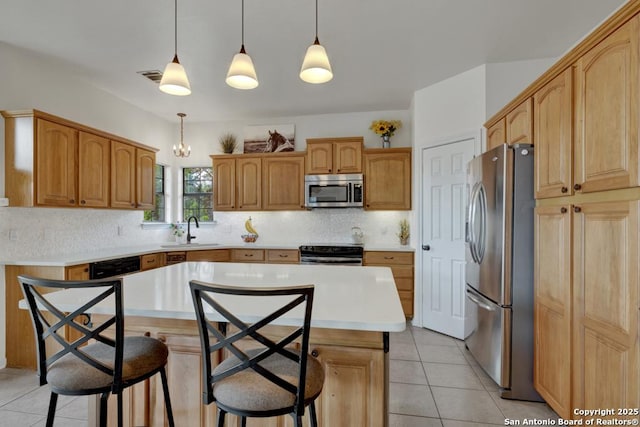 kitchen with a center island, sink, stainless steel appliances, decorative light fixtures, and a breakfast bar area